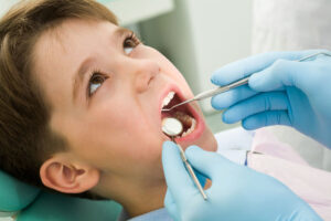 A young boy in a dentist's chair with a dental instrument in his open mouth.